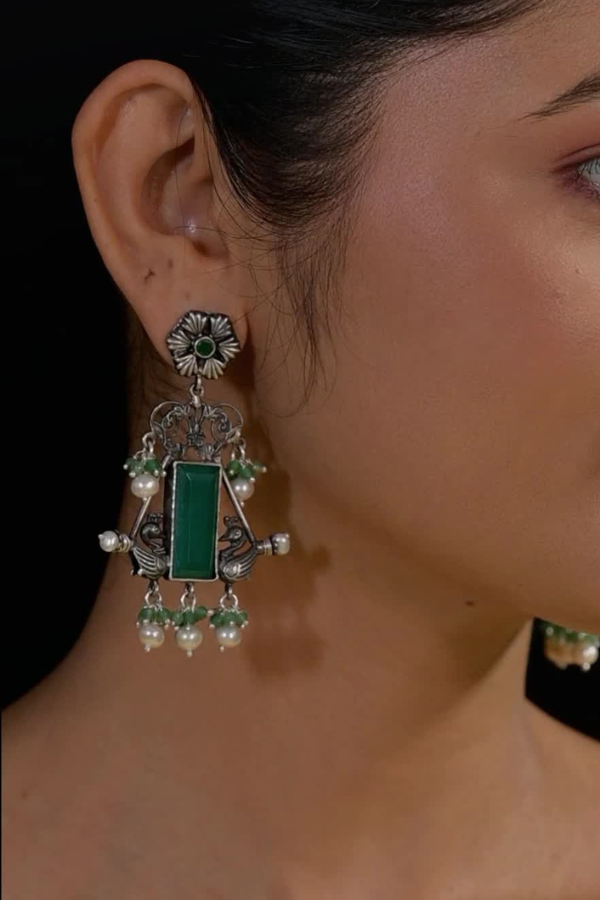 wearing a decorative earring with green gemstone and pearl-like beads.