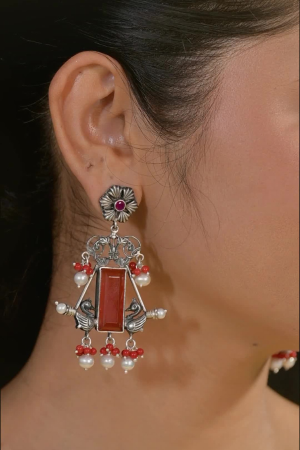 Earring with a red gemstone and pearl-like beads.